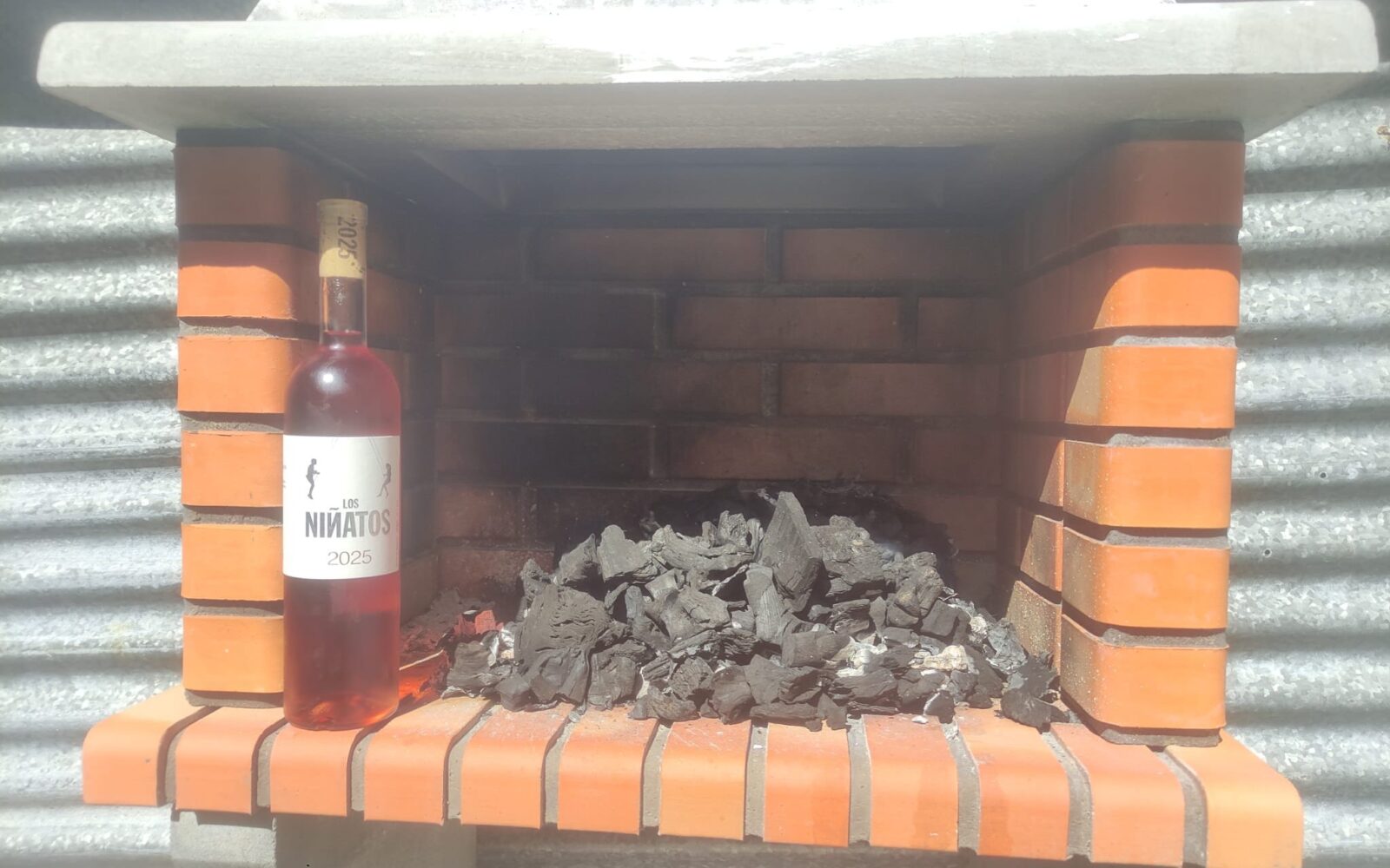 Botella del vino Los Niñatos 2025 delante de los carbones de una barbacoa